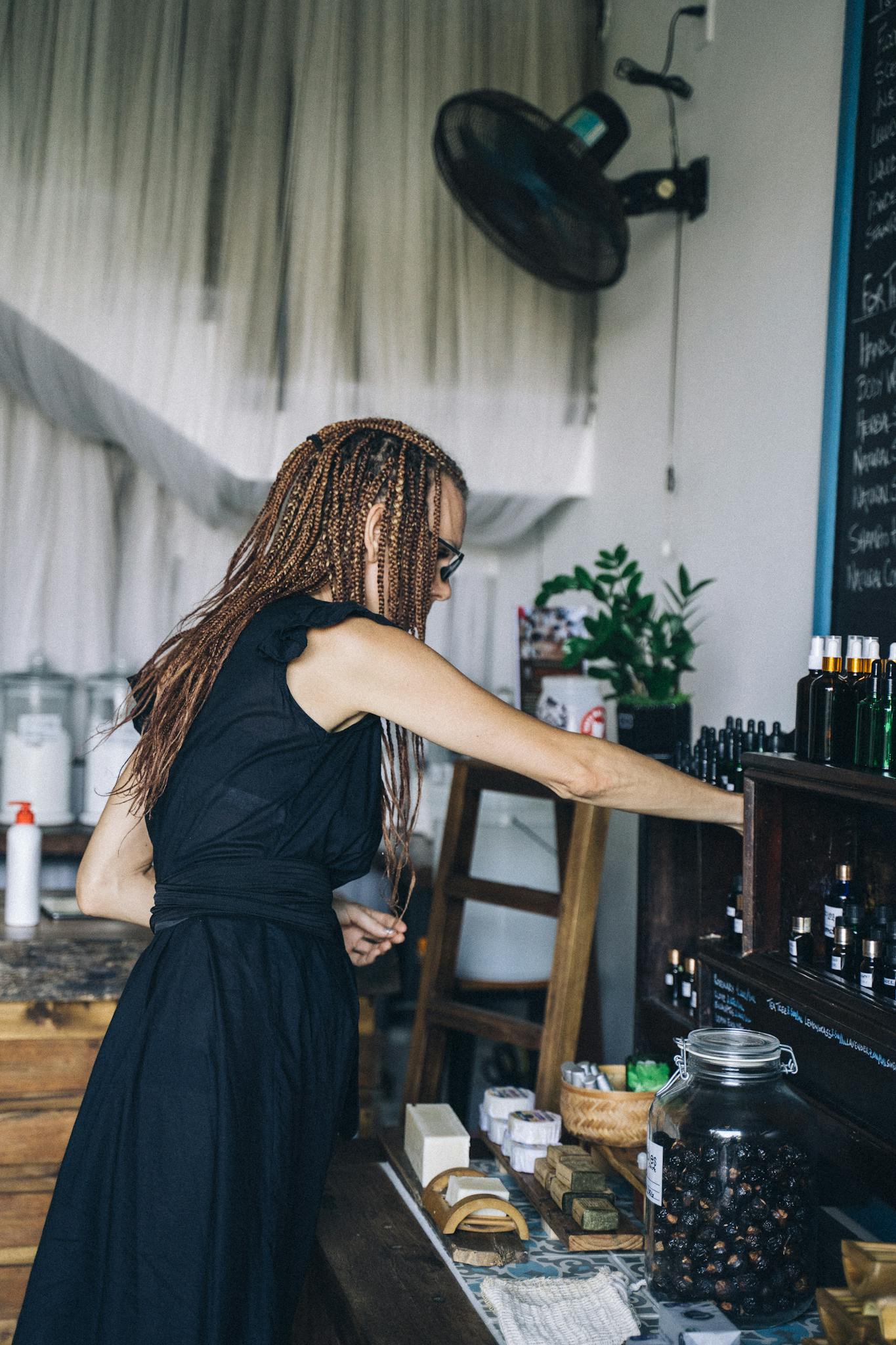 Side view of a woman with braids exploring items on a wooden shelf in a cozy indoor shop.