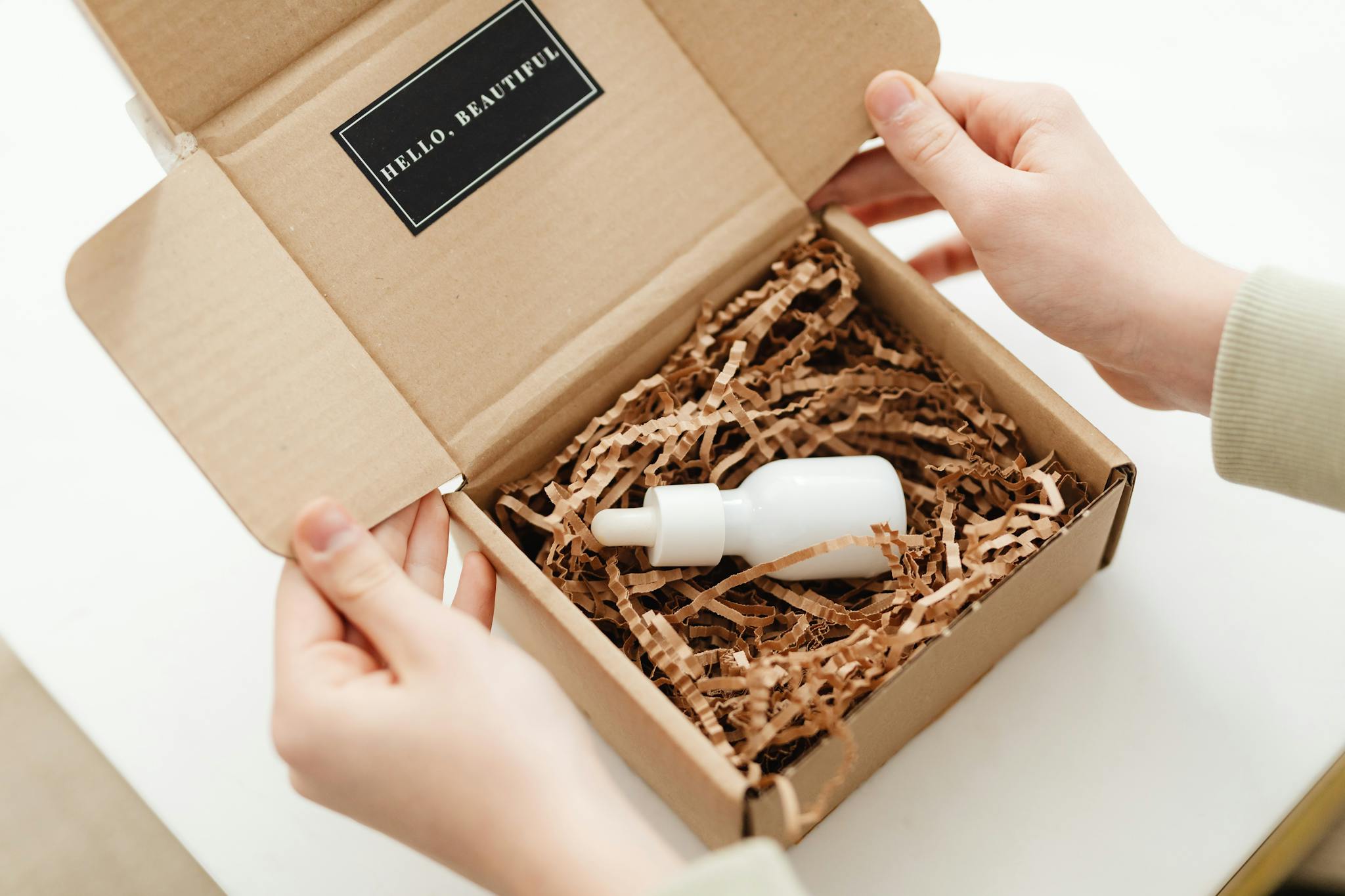 Hands opening a package with a skincare dropper bottle in protective packaging.